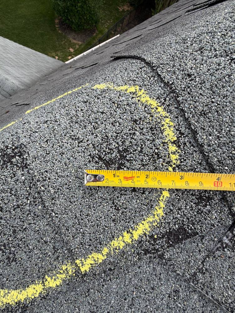 Close-up of hail damage bruise on asphalt shingle with chalk circle and tape measure, Northern Virginia roof inspection